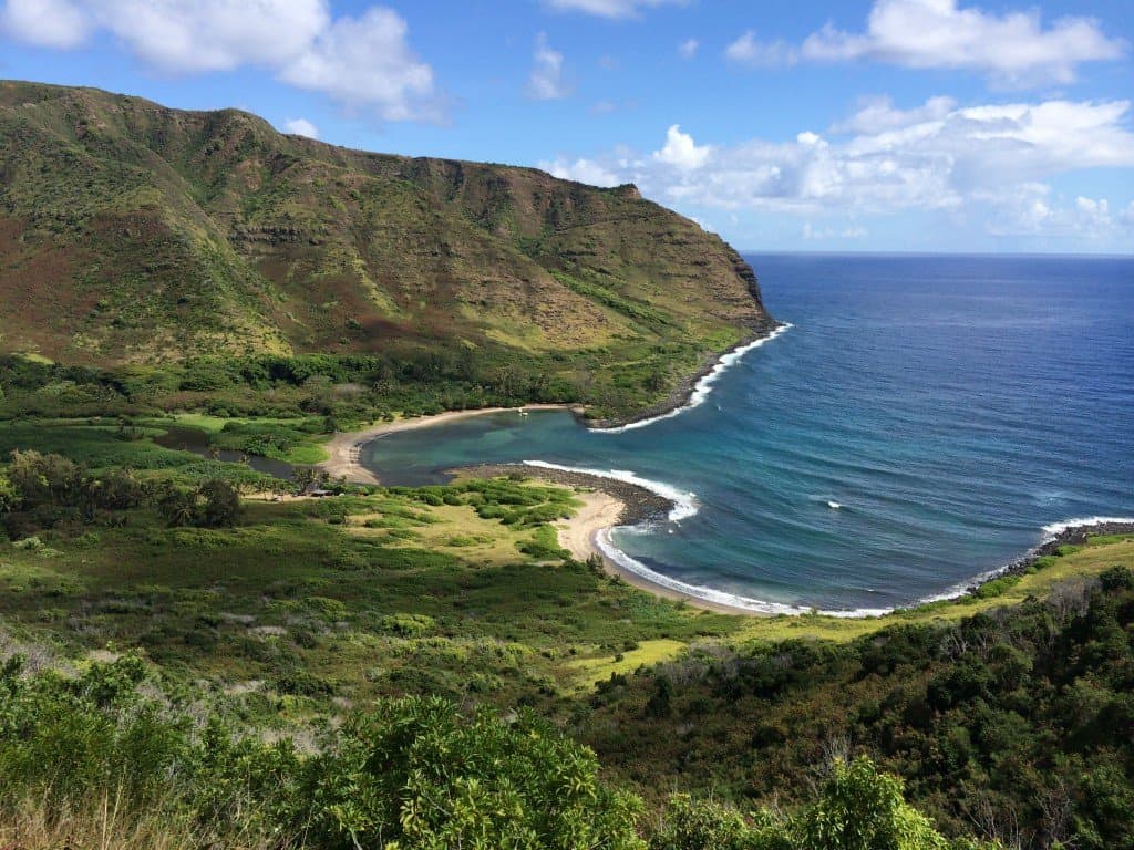 A sweeping Molokaʻi bay framed by green sea cliffs and a crescent beach